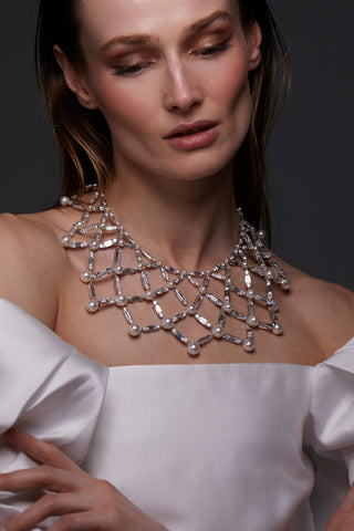 INGRID XL NETTING NECKLACE ON MODEL. SHE IS LOOKING DOWN WITH HER HAIR SLICKED BACK AND WEARING A WHITE OFF THE SHOULDER BRIDAL GOWN WITH PUFFY SLEEVES. 